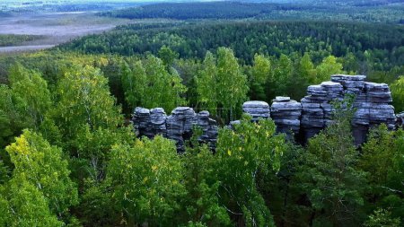 Aerial view of rock cliffs among green summer trees. Footage. Tops of the mountain cliffs in green forest