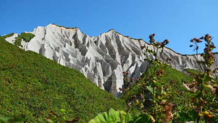 Amazing white mountains with green grass. Clip. Beautiful patterns on rocky white mountain with bright greenery on sunny summer day. White rocks of volcanic origin on island on summer day.