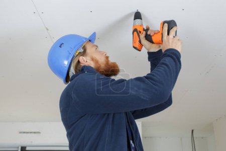 worker using a cordless drill on a plasterboard ceiling