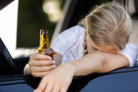 woman slumped over car window holding bottle of beer