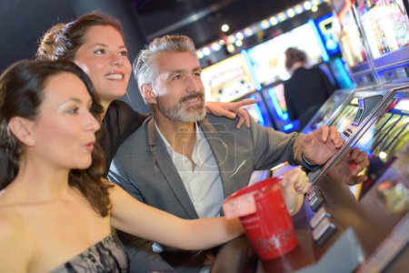 three adults sat excitedly around casino machine
