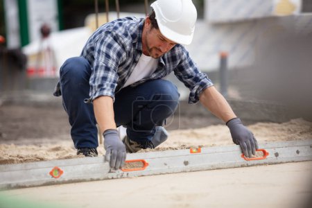 worker flattening freshly laid concrete outdoors with length of metal