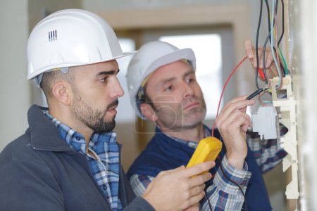 electricians checking socket voltage with digital multimeter two workers
