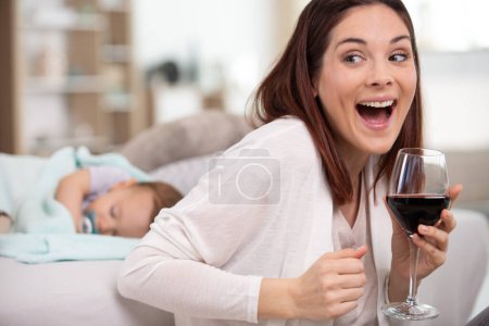 Mutter trinkt Glas Wein vor schlafendem Baby
