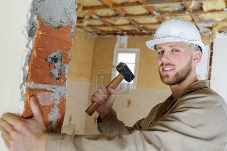 young builder using a hammer to remove walls plaster