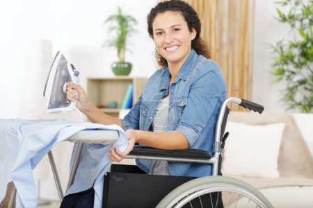 happy woman in a wheelchair ironing at home