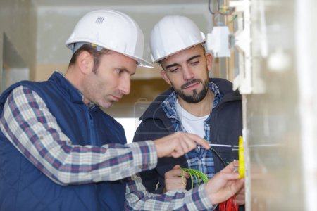 zwei Bauarbeiter in Helmen arbeiten mit Strom in Innenräumen