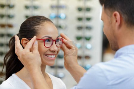 optician fitting glasses on beautiful young woman