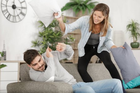 attractive couple fighting with pillows in living room