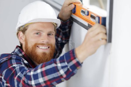 Trabajador de la construcción utilizando el nivel de burbuja durante la instalación de ventanas en interiores
