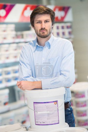 young man with paints standing near racks in paint store