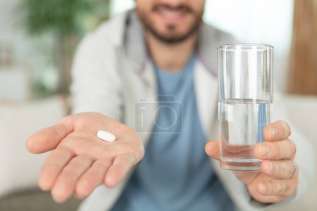 Junger Mann zeigt Pille und Glas Wasser