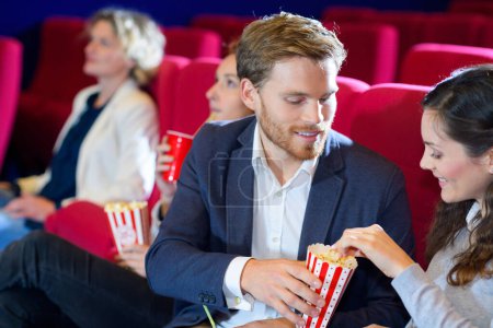 happy young couple eating popcorns at the cinema