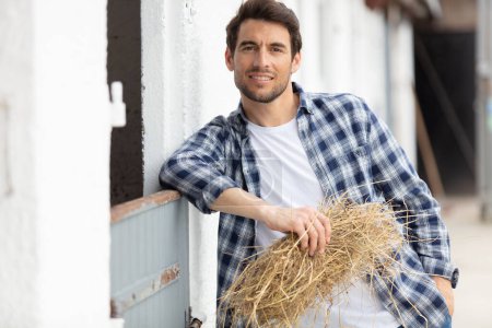 portrait of a smiling man holding hay in a stable