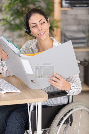 Frau im Rollstuhl mit Kopfhörer schaut in Ordner