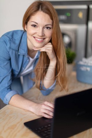 retrato de la joven feliz con el ordenador portátil en la lavandería
