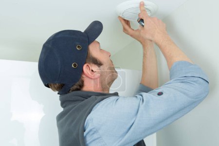 technician installing smoke detector on ceiling wall