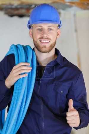 tradesman with reel of cable on shoulder giving thumbs up