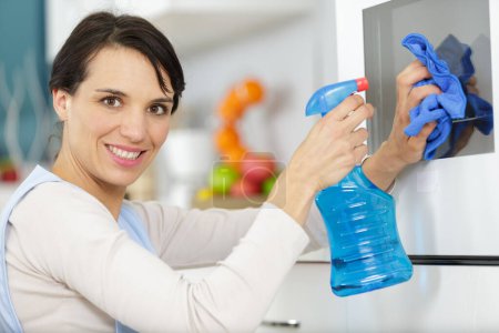 glückliche Frau putzt Küchentuch und sprüht in Küche