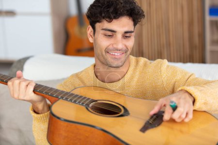 young man with guitar on sofa in room