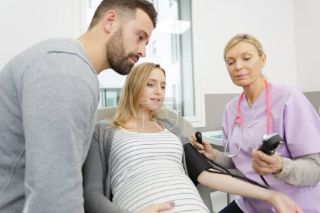 nurse measuring blood pressure of pregnant woman with husband present