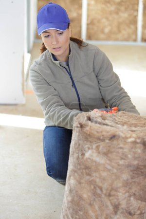 Frau benutzt Rolle Mineralwolle auf dem Holzboden