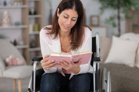 Lächelnde junge Frau im Rollstuhl liest Buch