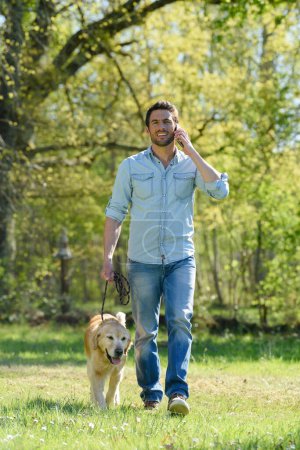 Mann geht mit Labrador-Hund spazieren und spricht mit Smartphone