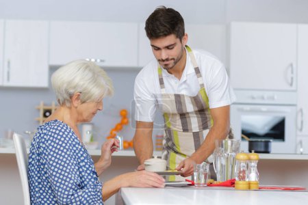 young man home help serving breakfast to senior lady