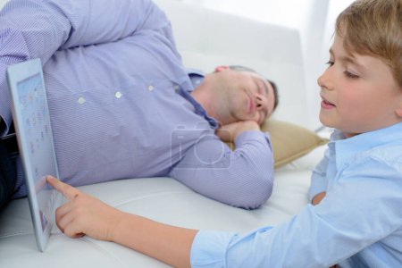 Child using tablet while adult sleeps