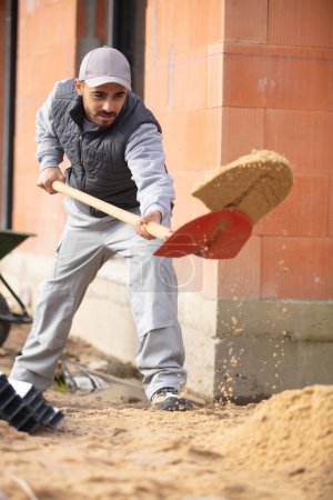 Männlicher Bauunternehmer schaufelt Sand auf die Bebauung