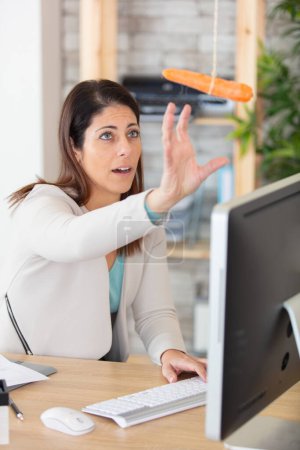 trabajadora de oficina alcanza para zanahoria colgando por encima de la computadora