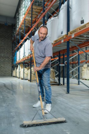 mature man sweeping warehouse floor