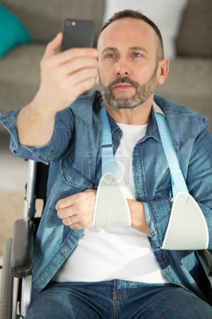 Mann im Rollstuhl mit Arm im Tragetuch macht Selfie