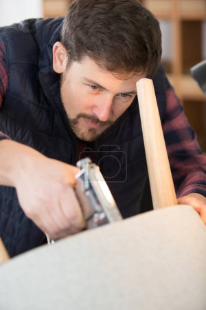 Männlicher Handwerker mit Klammerpistole auf Stuhlsockel