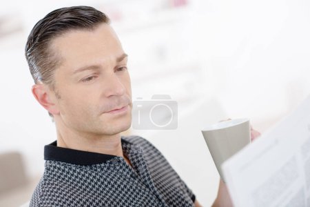 smart man sat holding cup and reading newspaper