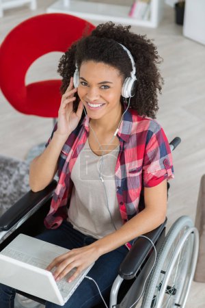 young disabled girl in wheelchair using laptop and headphones