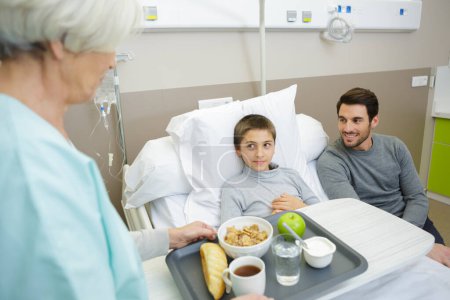 Niño pequeño con goteo intravenoso comiendo sopa en la cama del hospital
