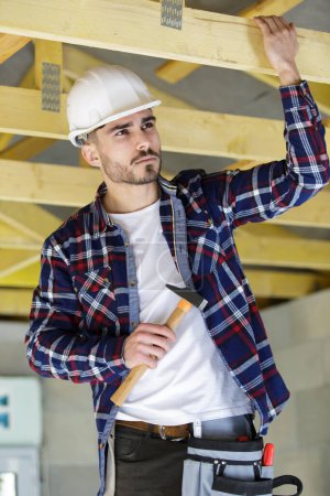 male builder on the roof of a wooden frame house