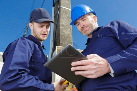 trabajadores electricistas inspeccionando contador eléctrico al aire libre