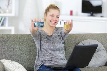 femme utilisant un ordinateur portable à la maison tenant cadenas et carte bancaire