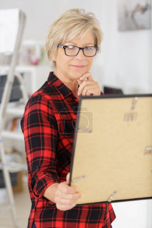 mature woman at home holding a painting