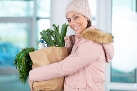 Lächelnde junge Hausfrau mit Einkaufstüte voller Gemüse