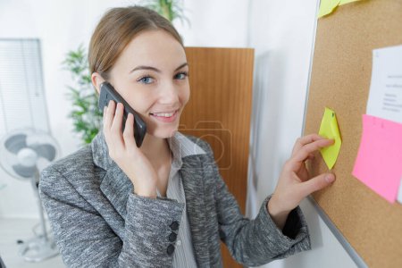 woman on telephone putting post-it note on to board