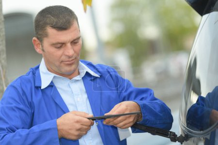 worker checking rear windscreen wiper blade on car