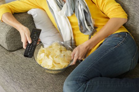 woman on sofa eating crisps while watching tv