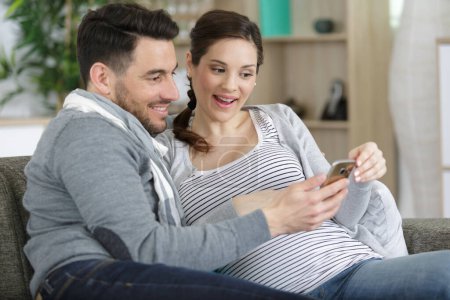 Glückliche Schwangere nutzen Smartphone zu Hause