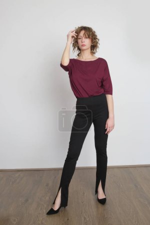 Photo for Serie of studio photos of young female model wearing simple comfortable outfit, organic cotton burgundy blouse and black skinny trouserswith slits - Royalty Free Image