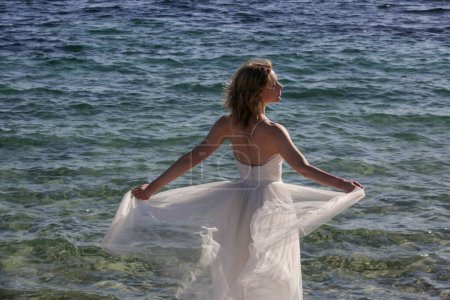 Photo for Portrait of the bride in long white wedding dress with ocean water in the backgound - Royalty Free Image