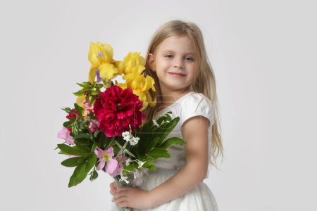 Studio portrait of beautiful little girl holding big colorful bouquet of various flowers.